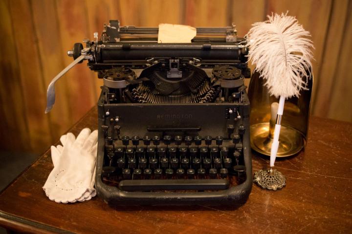 black typewriter on top of wooden table with feather pen next to it